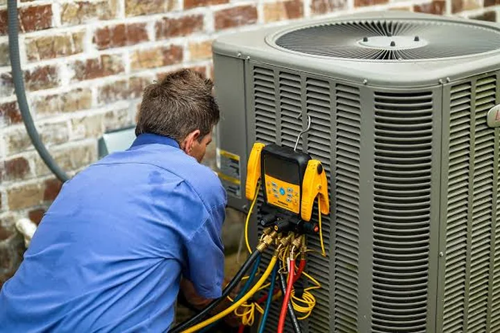 HVAC maintenance technician checking refrigerant gauges on a condenser